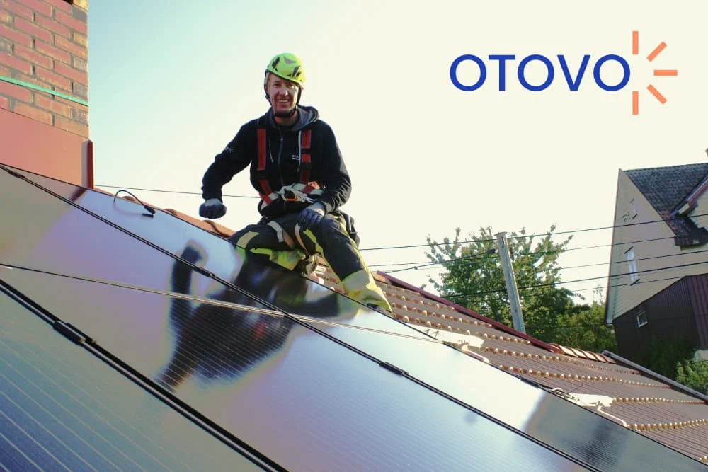 Person auf Dach installiert Solarmodule. Das Logo der Marke otovo ist abgebildet